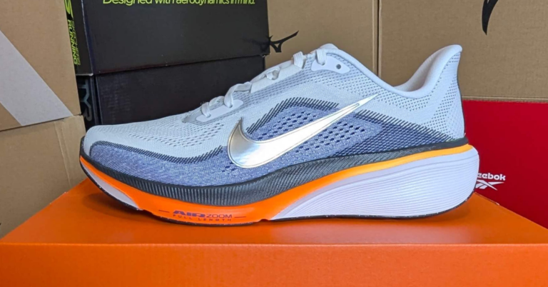 Nike running shoe with a silver Swoosh on a grey knit upper and bright orange midsole, resting on an orange box.