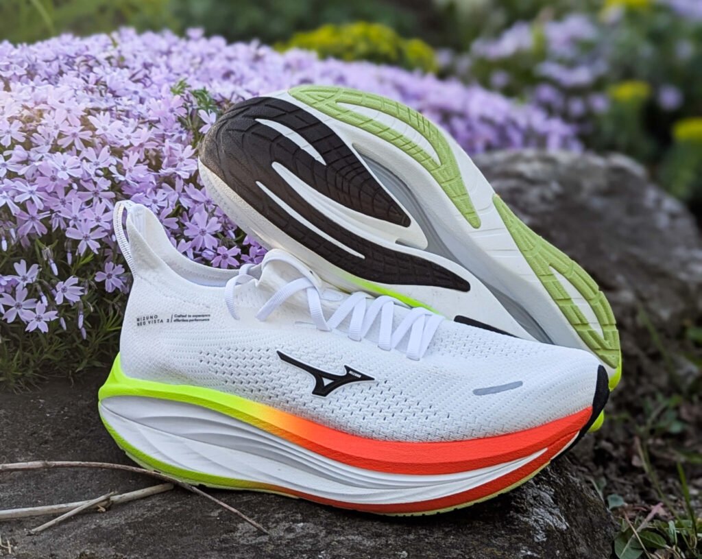 Close-up of a Mizuno neo vista 3 with neon green and orange sole resting on a rock beside purple flowers in a garden setting.