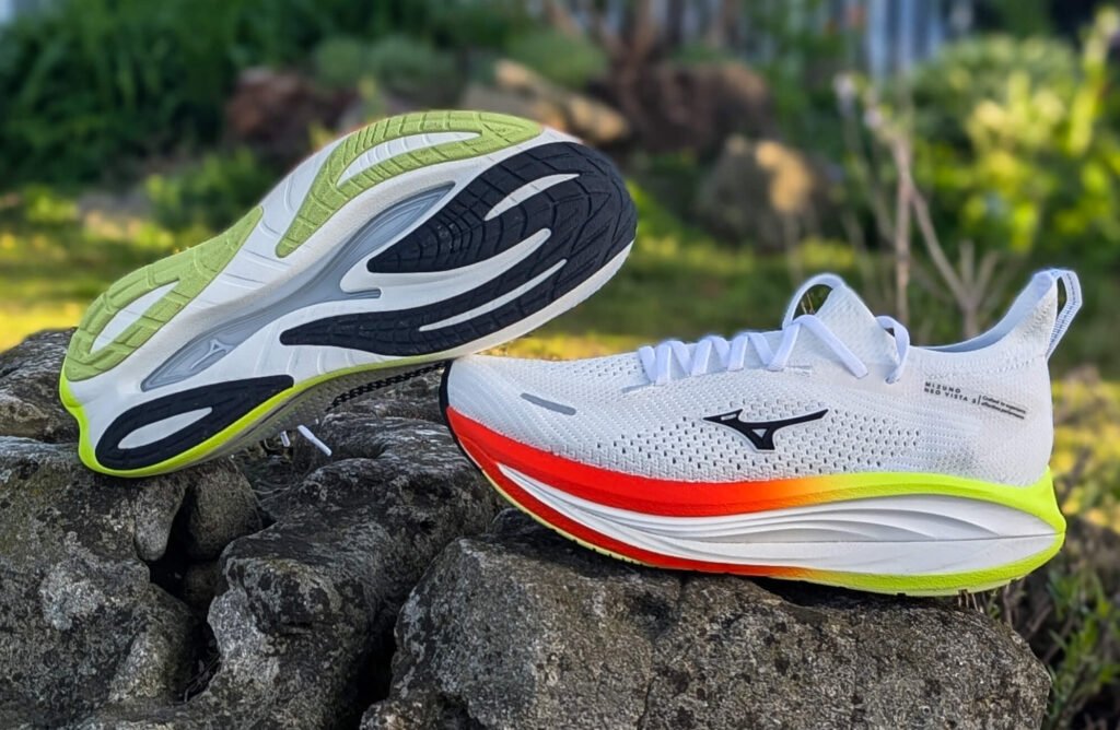 Mizuno neo vista 3 with neon green and bright orange soles resting on a rocky surface outdoors.